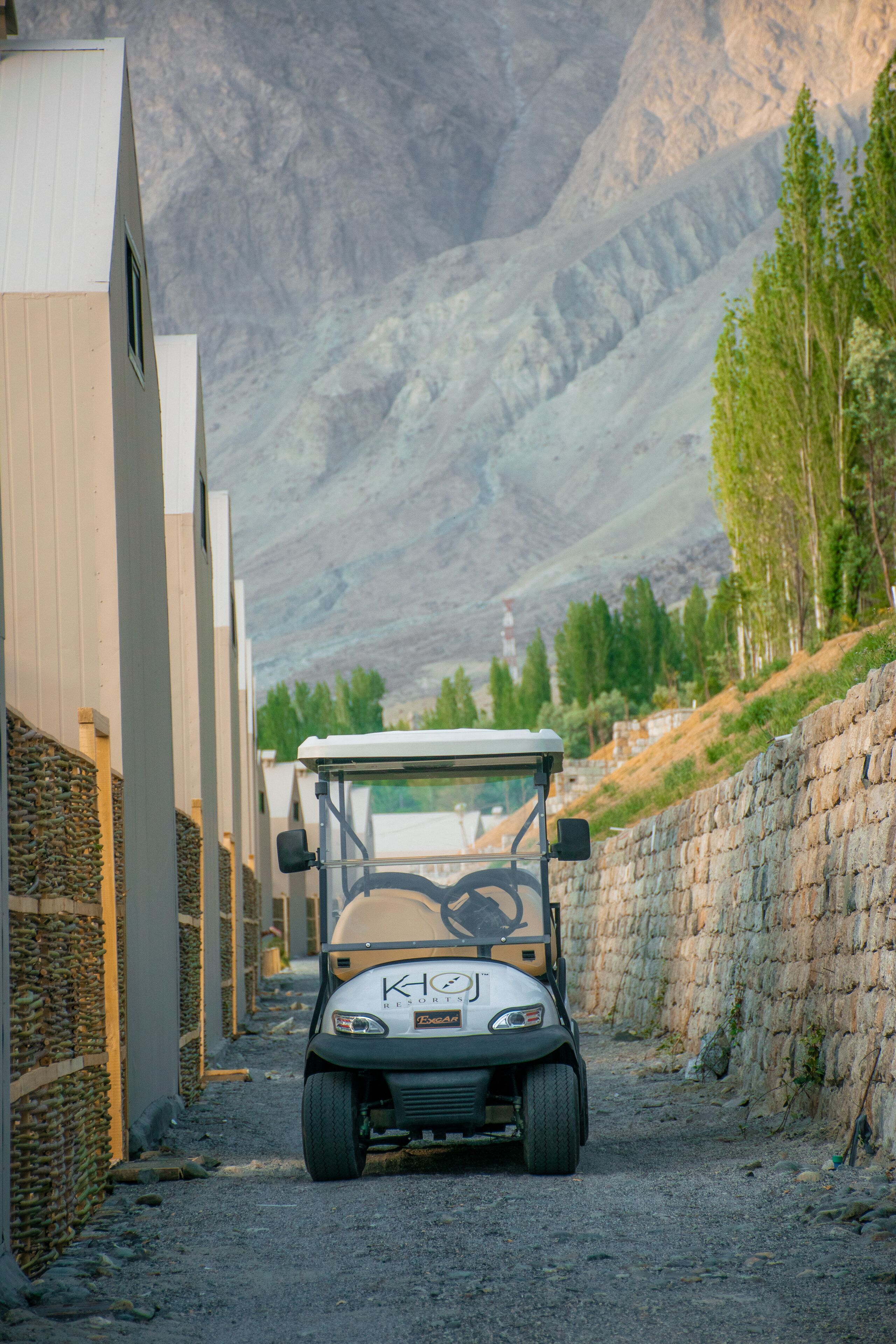 A golf cart parked on a gravel path beside a building with a mountainous backdrop.