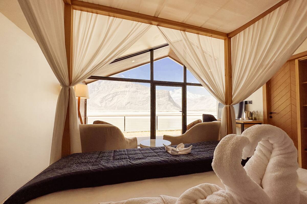 Ein Schlafzimmer mit großem Fenster, einem Bett, einem Sessel und einem Tisch.