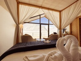 A bedroom with a large window, a bed, a chair, and a table.