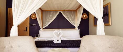 A bedroom with a canopy bed, two armchairs, a small round table, and a patterned rug.