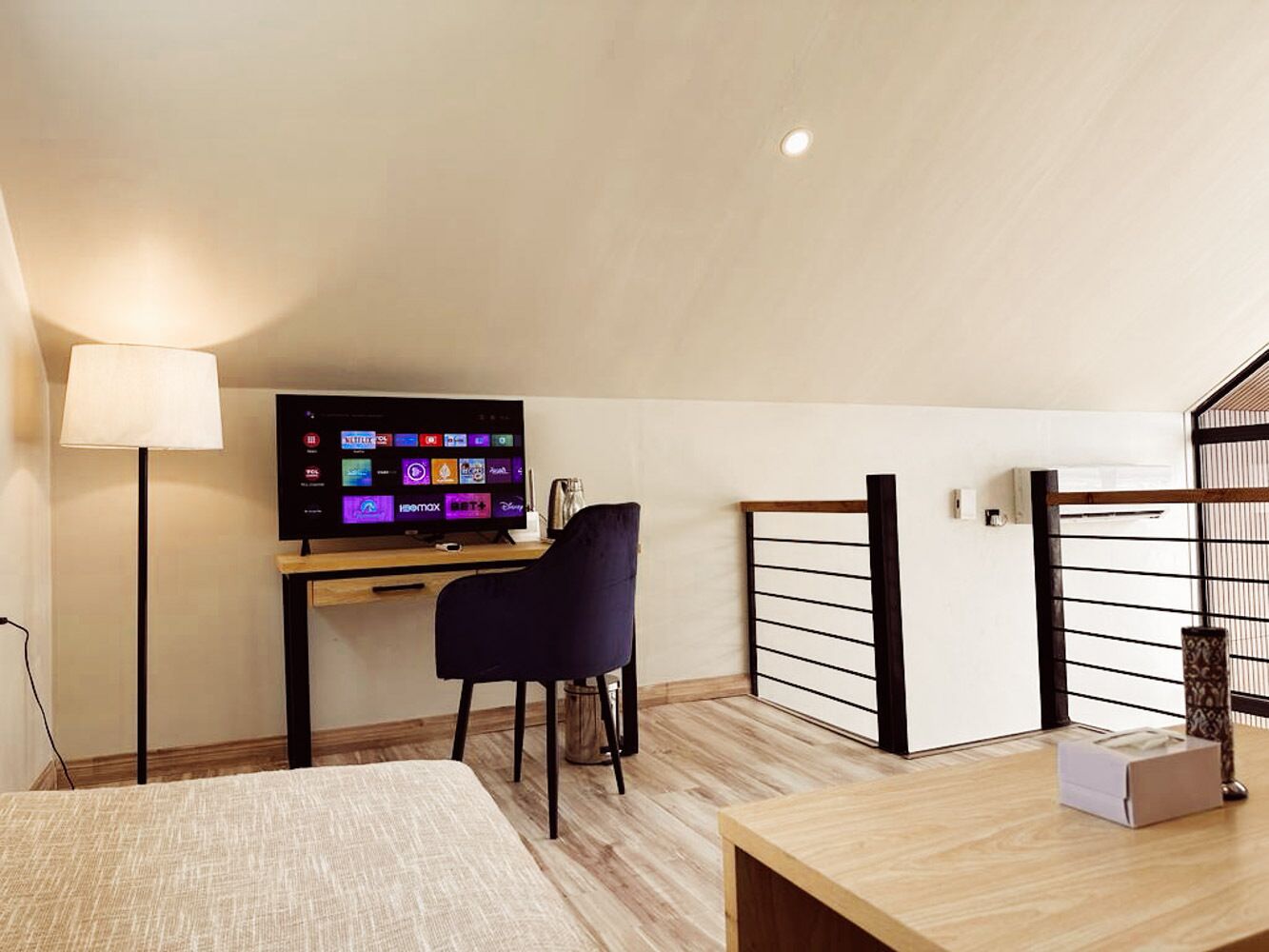 A modern room with a bed, a desk with a computer, a chair, and a television displaying streaming services.