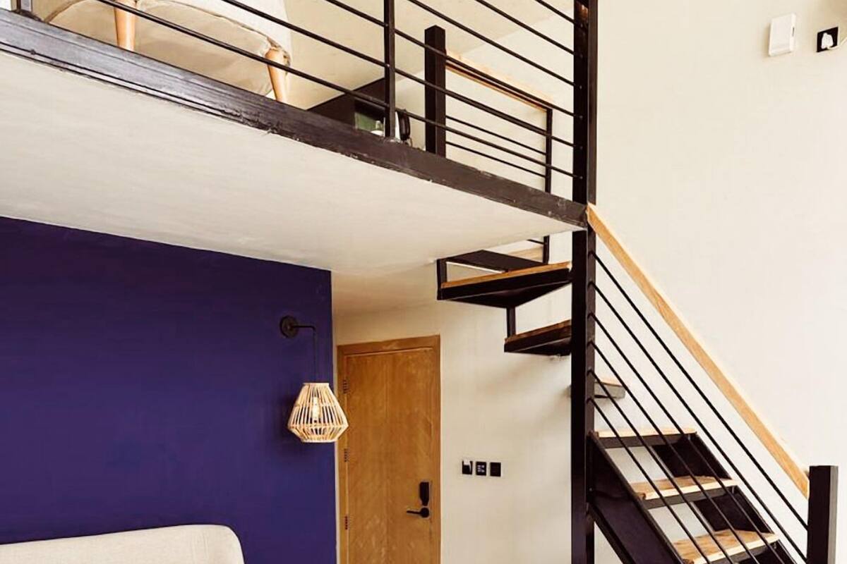 Ein Schlafzimmer mit Bett, einer Holzbank, einer Treppe mit schwarzen Geländern und einer Tür.