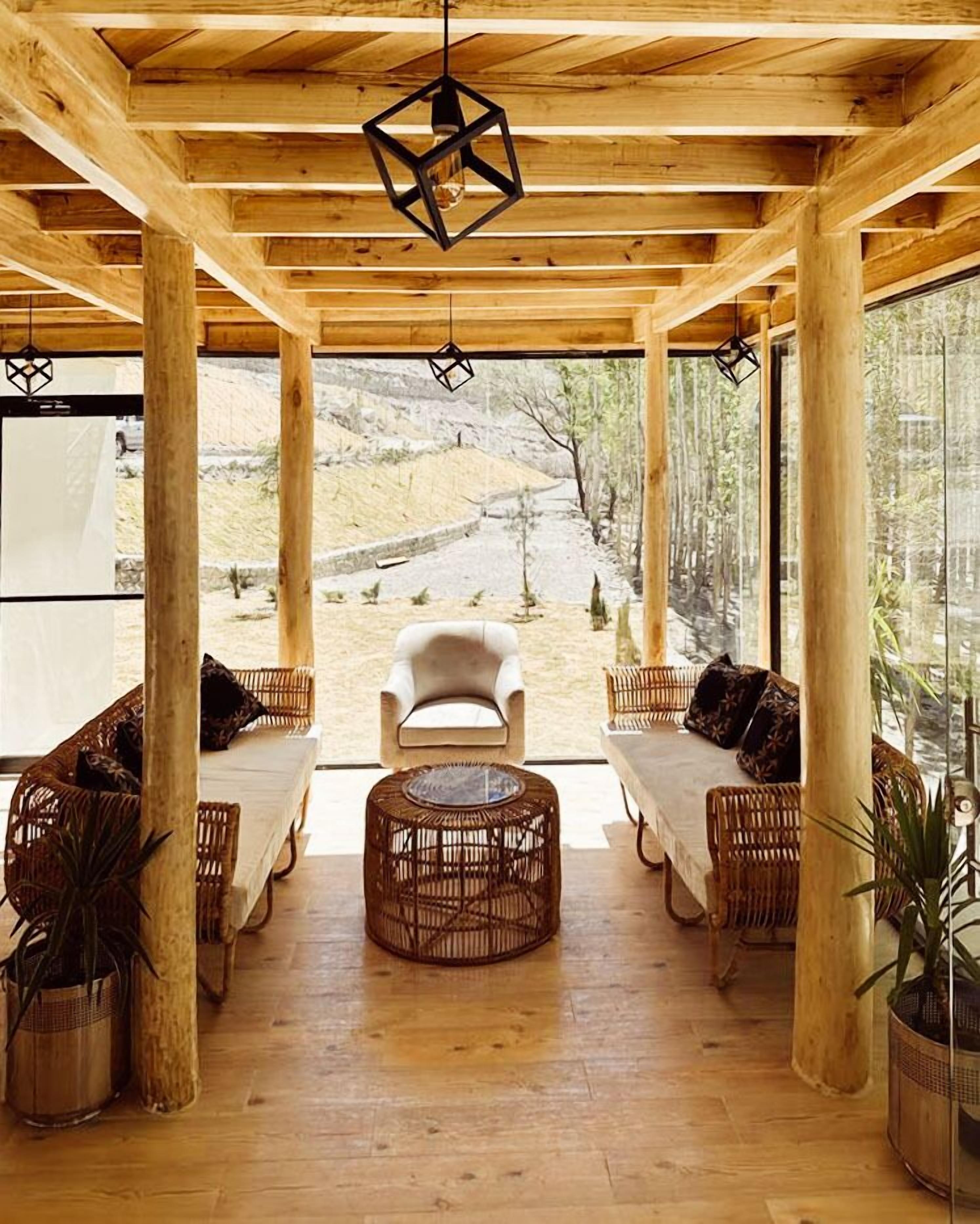 A wooden interior with a central seating area, large windows, and a view of a natural landscape.