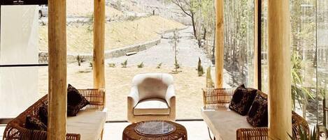 A wooden interior with a central seating area, large windows, and a view of a natural landscape.