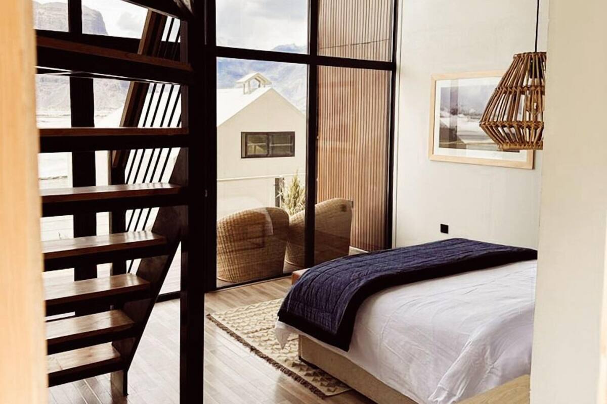 Ein Schlafzimmer mit einem großen Bett, einer Holztreppe und Blick auf Berge durch große Fenster.