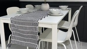 Ein Esstisch mit weißen Stühlen, einer schwarz-weißen Tischdecke und einem Blumentopf.