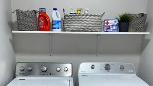 Zwei Maytag Frontlader-Waschmaschinen nebeneinander, darüber ein Regal mit Reinigungsmitteln.