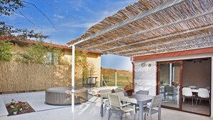 Une terrasse avec une table et des chaises, un jacuzzi et un espace abrité doté d’un toit en fibres tressées.