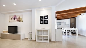 Un salon moderne avec un téléviseur à écran plat, une console blanche, un tableau représentant une orchidée et une étagère blanche.