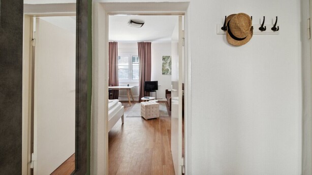A hallway leading to a bedroom with a bed, a small table, and a television. There is a hat on a wall-mounted rack. - Arbio I Cozy apartment near Ku`damm (Berlin)