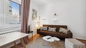 A modern living room with a brown sofa, white coffee table, and a view of a cityscape through a window. - Arbio I Cozy apartment near Ku`damm (Berlin)