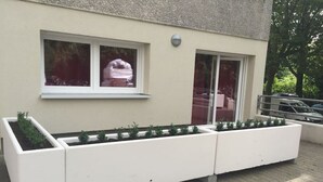 Een witte plantenbak met planten, voor een gebouw met ramen en een deur.