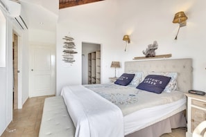 Quarto com cama, mesas de cabeceira, luminárias fixadas na parede e uma porta.