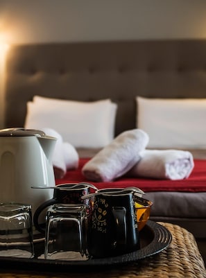 A hotel room with a bed, a tray with coffee cups, a teapot, and rolled towels.