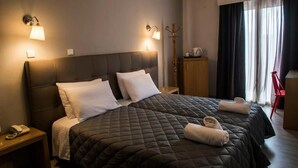 A hotel room with a large bed, two bedside lamps, a wooden nightstand with a telephone, a wooden cabinet, and a red chair. - HOTEL MINOS (Preveza)