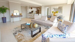 A modern living room with a sofa, coffee table, and a dining area with chairs. - Azalia Apartments (Sandton)