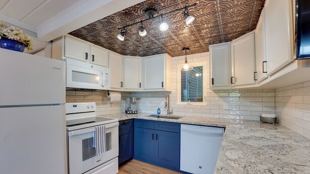 A modern kitchen with white cabinetry, a granite countertop, and a decorative ceiling. - Big Pine Island Lake Cottage w/ Boat Dock & Kayaks (Belding)