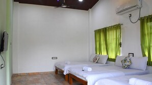 Ein Hotelzimmer mit zwei Einzelbetten, einem Deckenventilator, einer Klimaanlage und grünen Vorhängen.