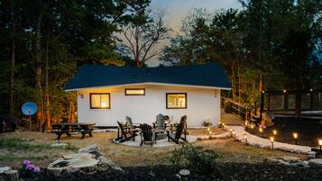A small house with a dark roof, a picnic table, and outdoor seating.