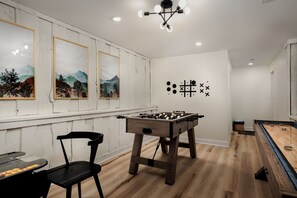 Una habitación con mesa de futbolín, una mesa con sillas y cuadros en la pared.