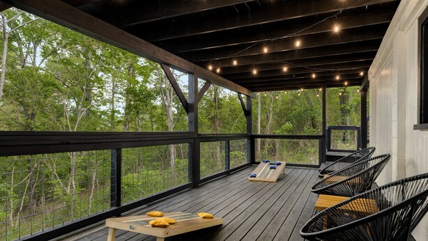 A covered deck with a wooden table, black chairs, and a view of trees. - Lake-view! Hot Tub! Fire Pit. Grill. Game Room. King bed. (Luray)