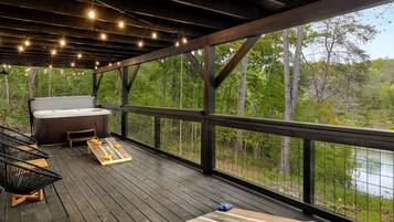 A wooden deck with a hot tub, seating area, and a view of a forest and river.