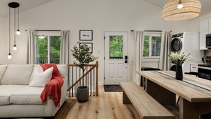 A modern living room with a sofa, a dining table, and a kitchen area with a washing machine. - Lake-view! Hot Tub! Fire Pit. Grill. Game Room. King bed. (Luray)