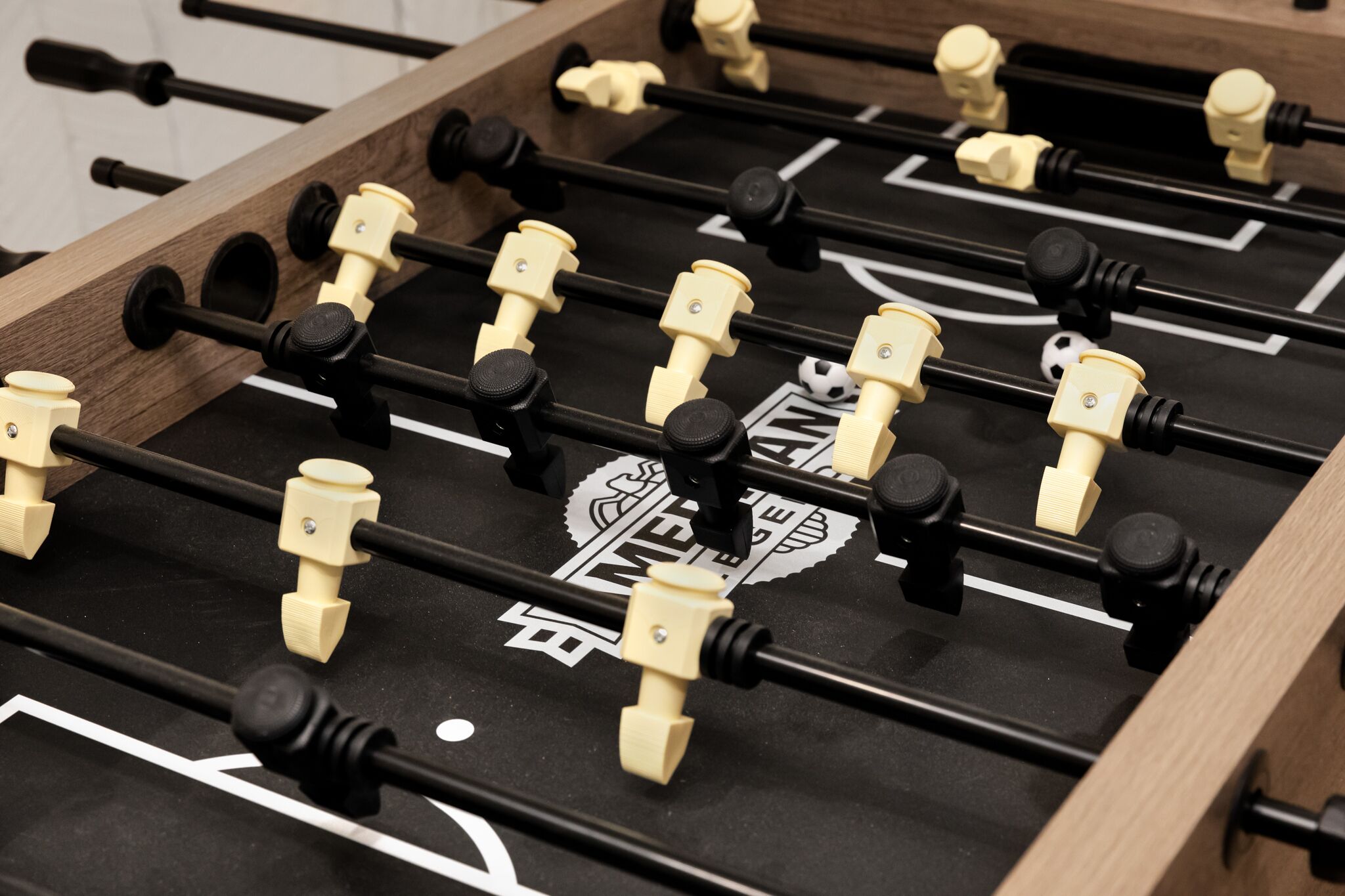 A close-up of a foosball table with a wooden frame and black playing surface.