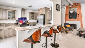Cozinha moderna com bancadas de granito, eletrodomésticos de aço inoxidável e banquetas de madeira.