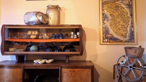 A wooden cabinet with glassware and metal containers, a vintage wheel, and two framed landscape paintings. - Tobia's House  (Giuggianello)