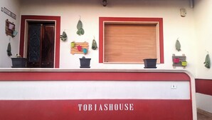 A building facade with a red and white color scheme, a wooden shutter door, and several potted plants. - Tobia's House  (Giuggianello)