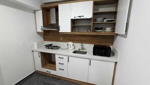 A compact kitchen with white cabinets, a microwave, a kettle, and a sink. - Çamlık Apart (Ayvalik)