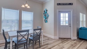 A dining area with a table and chairs, a decorative wall piece, and a door with a sign. - Get ready to enjoy Sunny Daze on the coast (Rockport)