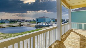 A covered balcony with a view of a small water body and a blue building in the background. - Get ready to enjoy Sunny Daze on the coast (Rockport)