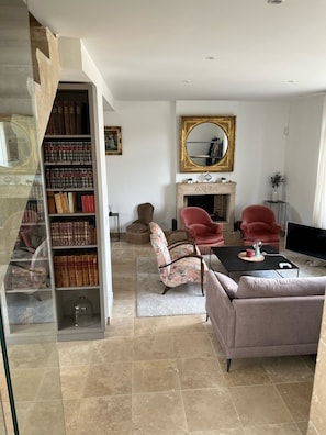 A living room with a fireplace, a bookshelf, and two red chairs. - Villa Dexception à 500m de la Plage (Merville-Franceville-Plage)