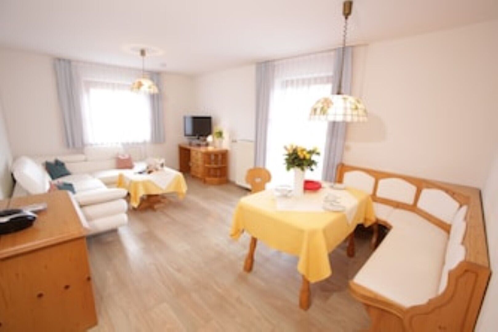 A well-lit, modern living room with a sofa, a dining table with yellow tablecloth, and a TV in the background.
