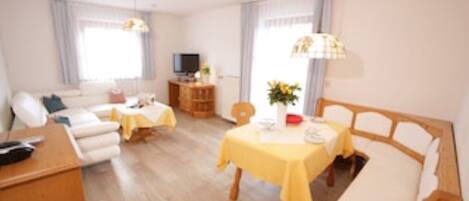 A well-lit, modern living room with a sofa, a dining table with yellow tablecloth, and a TV in the background.