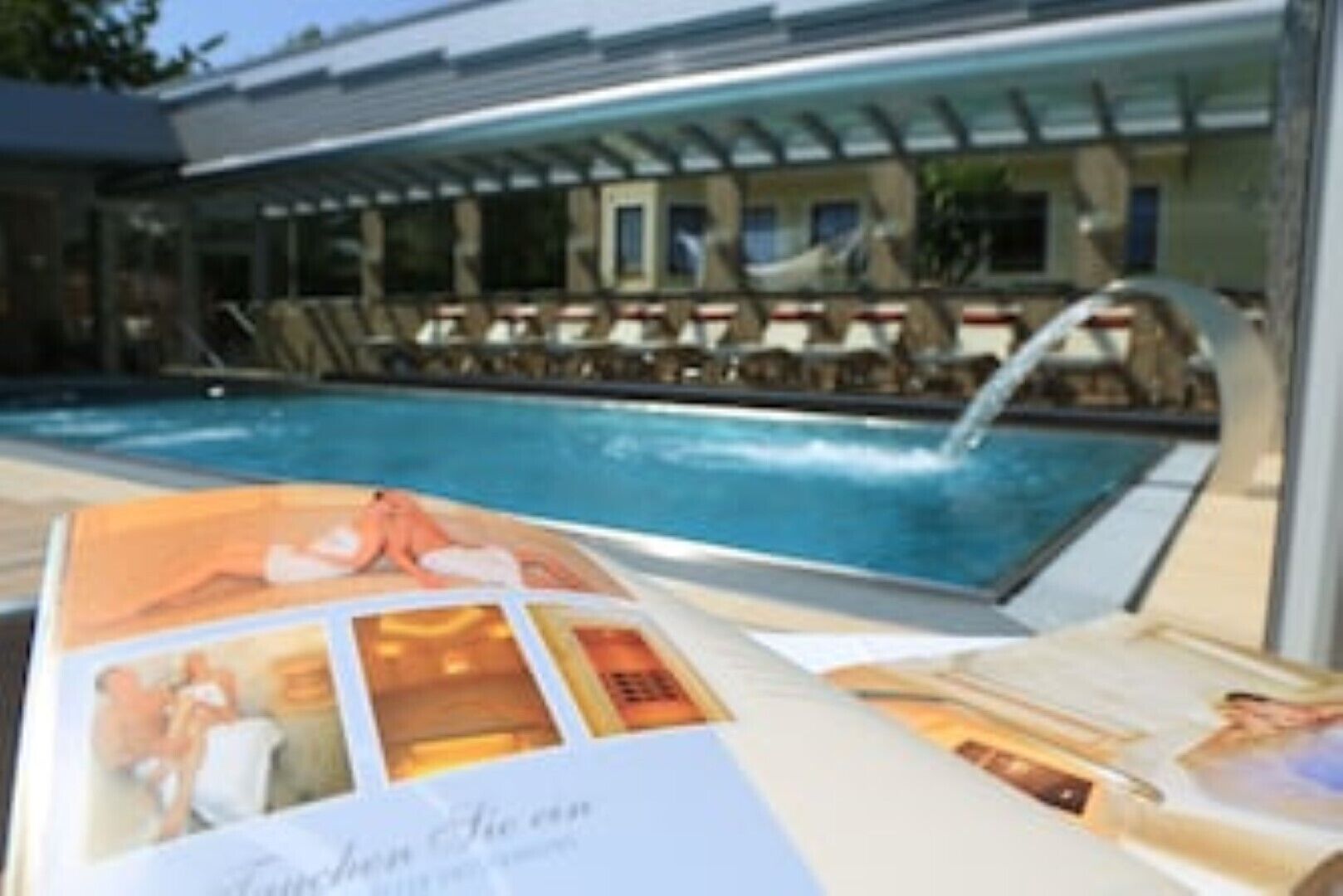 A swimming pool with a water feature, lounge chairs, and a covered seating area.