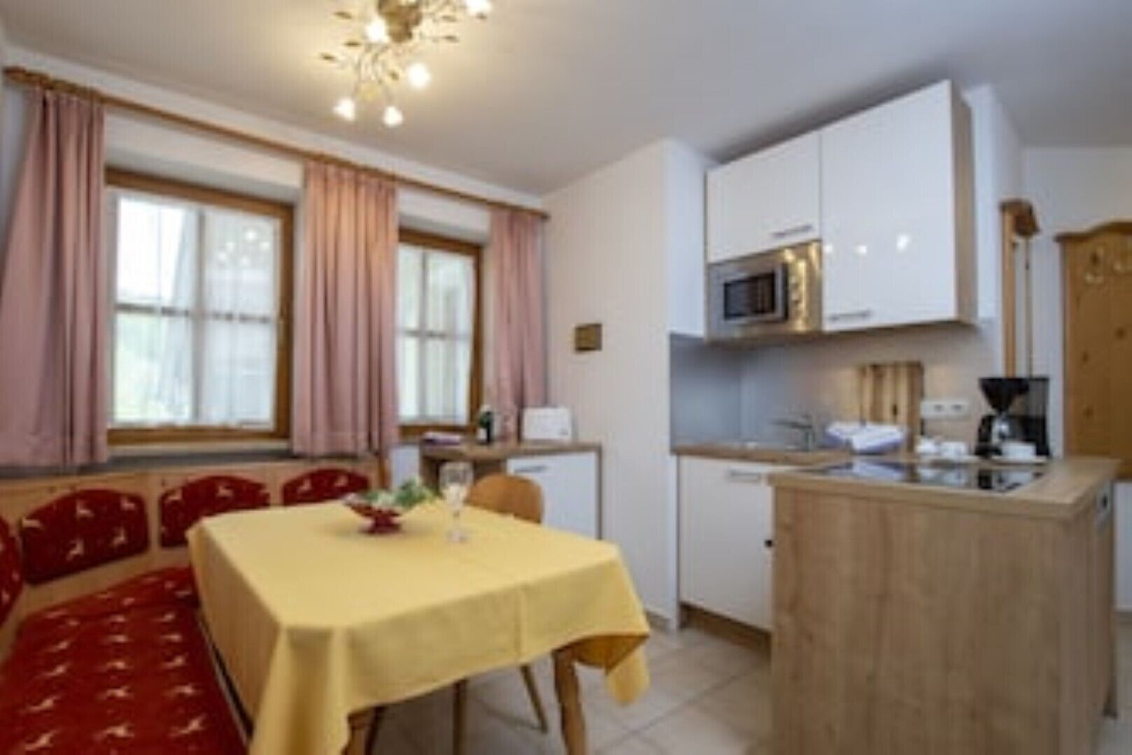 Een compacte keuken met witte kastjes, een magnetron en een koffiezetapparaat. Er is een eethoek met een tafel en stoelen.