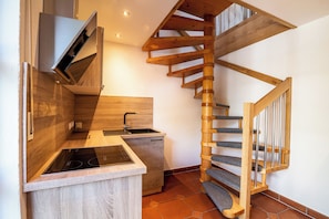 A kitchen with a built-in stove, a wooden staircase, and a small countertop.