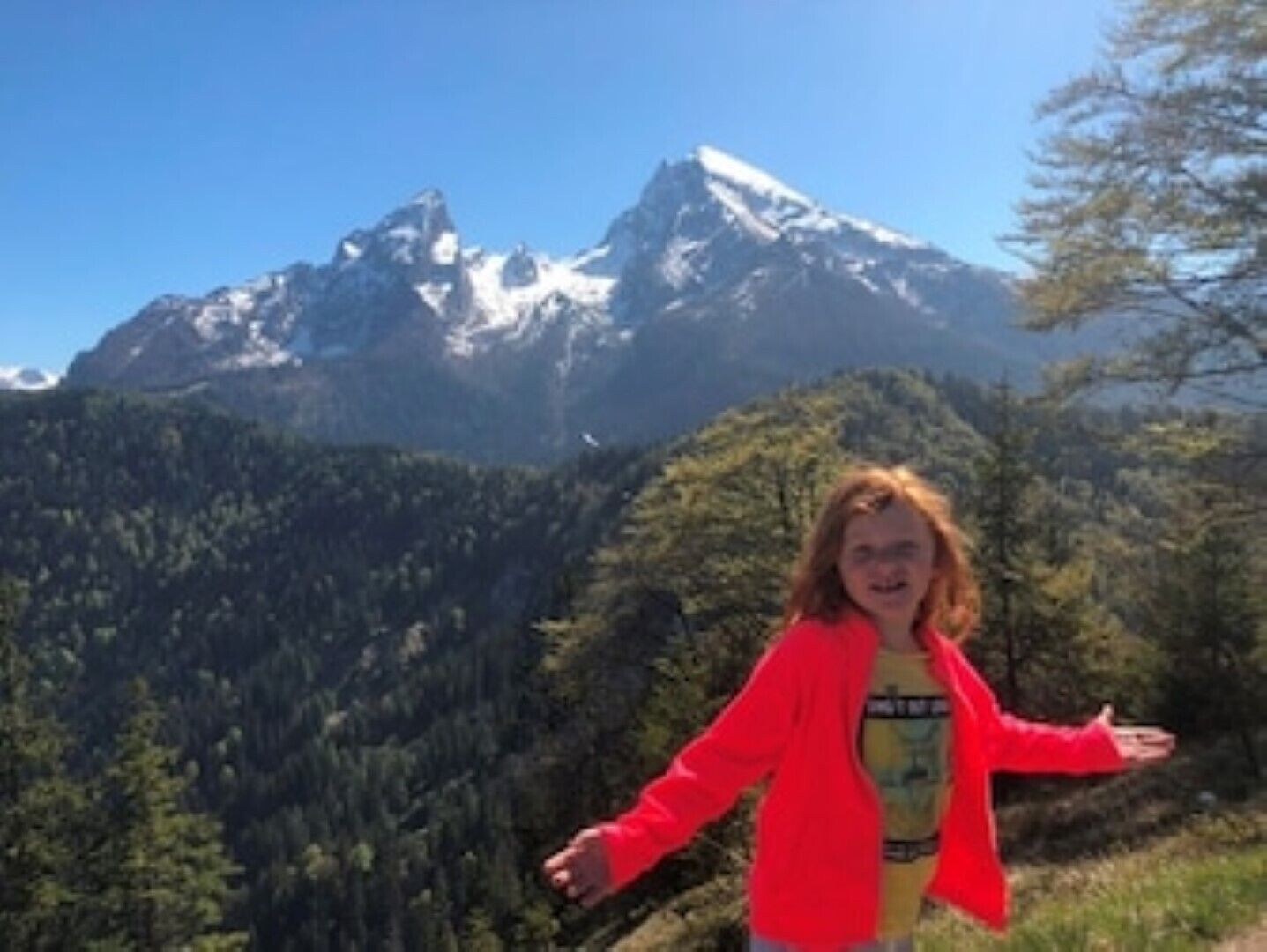 A person standing with arms outstretched in front of a mountain range.