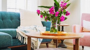 A living room with a teal sofa, a pink armchair, and a wooden coffee table with a vase of pink flowers. - Sea Street - Holiday stays at the beach! (St. Augustine Beach)