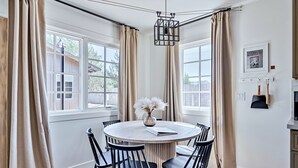 Un coin repas comprenant une table ronde, six chaises et un vase avec des fleurs séchées.