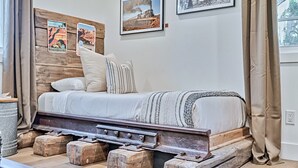 A bed with a wooden headboard, a metal frame, and a striped pillow. There are wooden blocks under the bed, and a window with curtains. - Inn History Grand Canyon Cabin 11 (Williams)