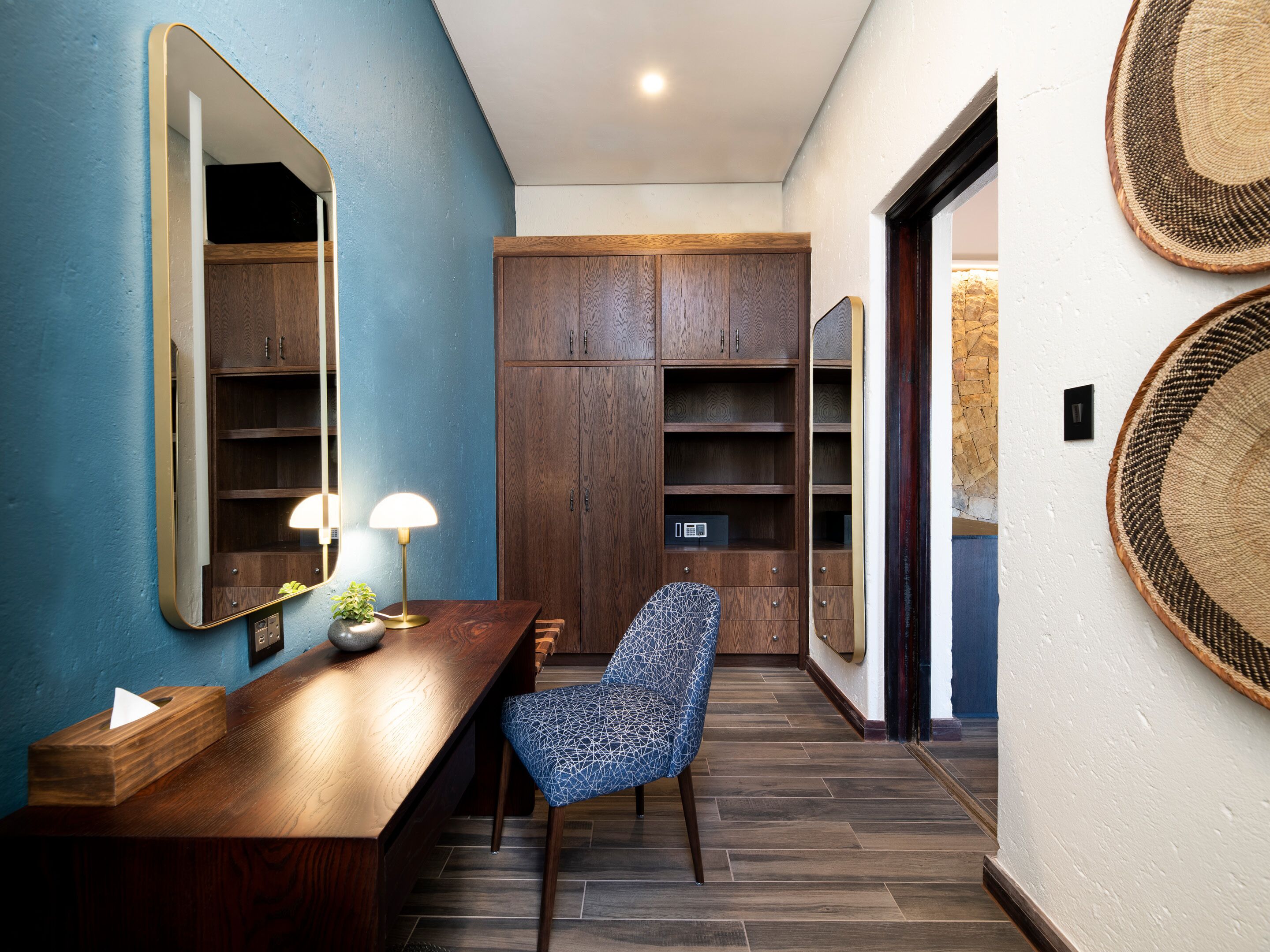A modern interior with a wooden desk, a chair, a large mirror, and a wardrobe.