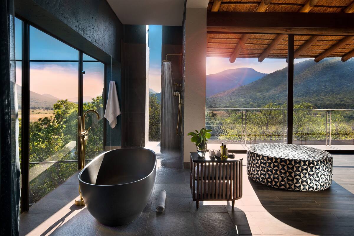 A modern bathroom with a large bathtub, a shower, and a view of a mountainous landscape.