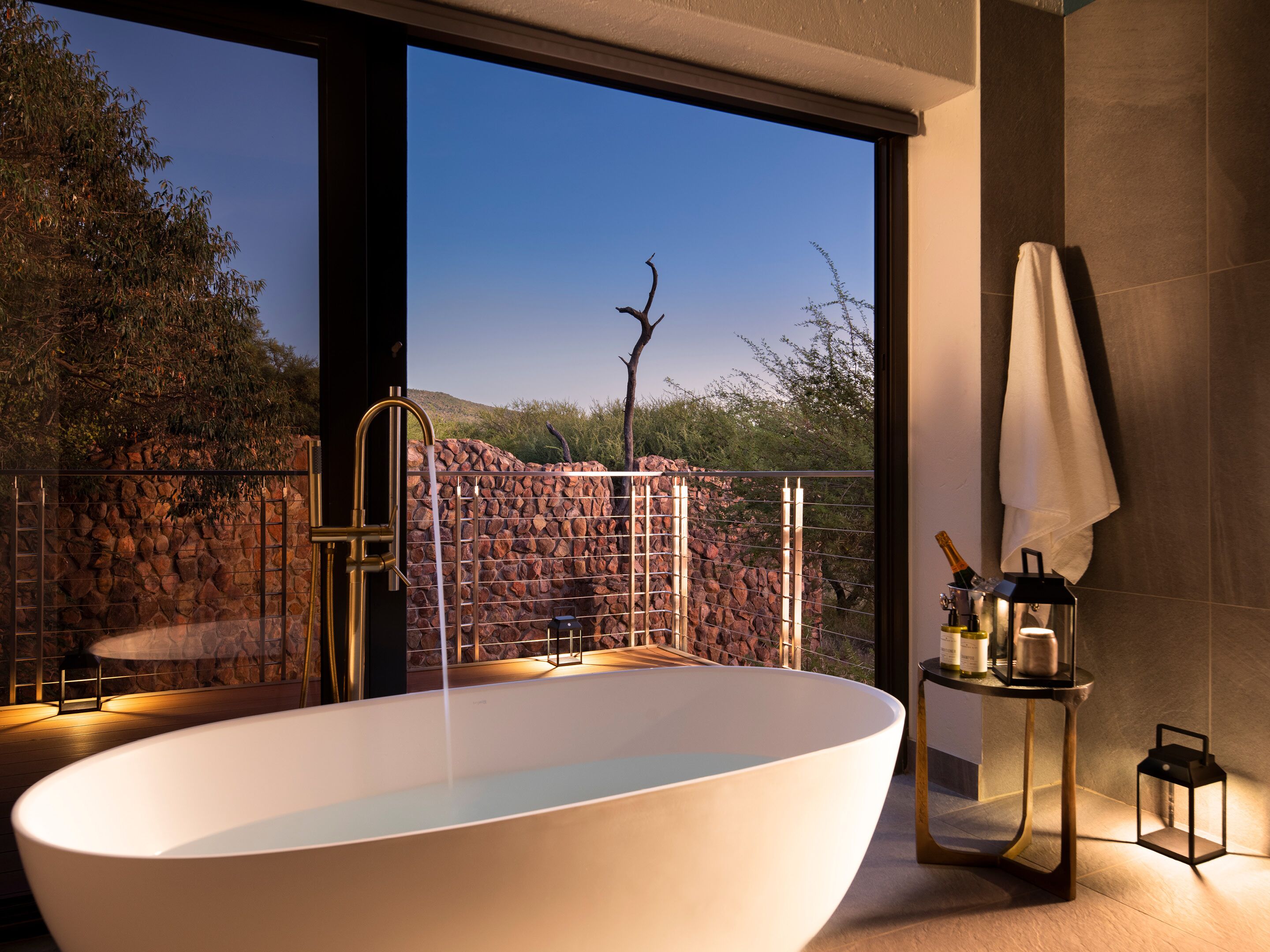 A modern bathroom with a freestanding bathtub, a stone wall, and a view of the outdoors.