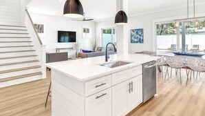Une cuisine moderne avec des meubles blancs, un îlot central et des luminaires suspendus.