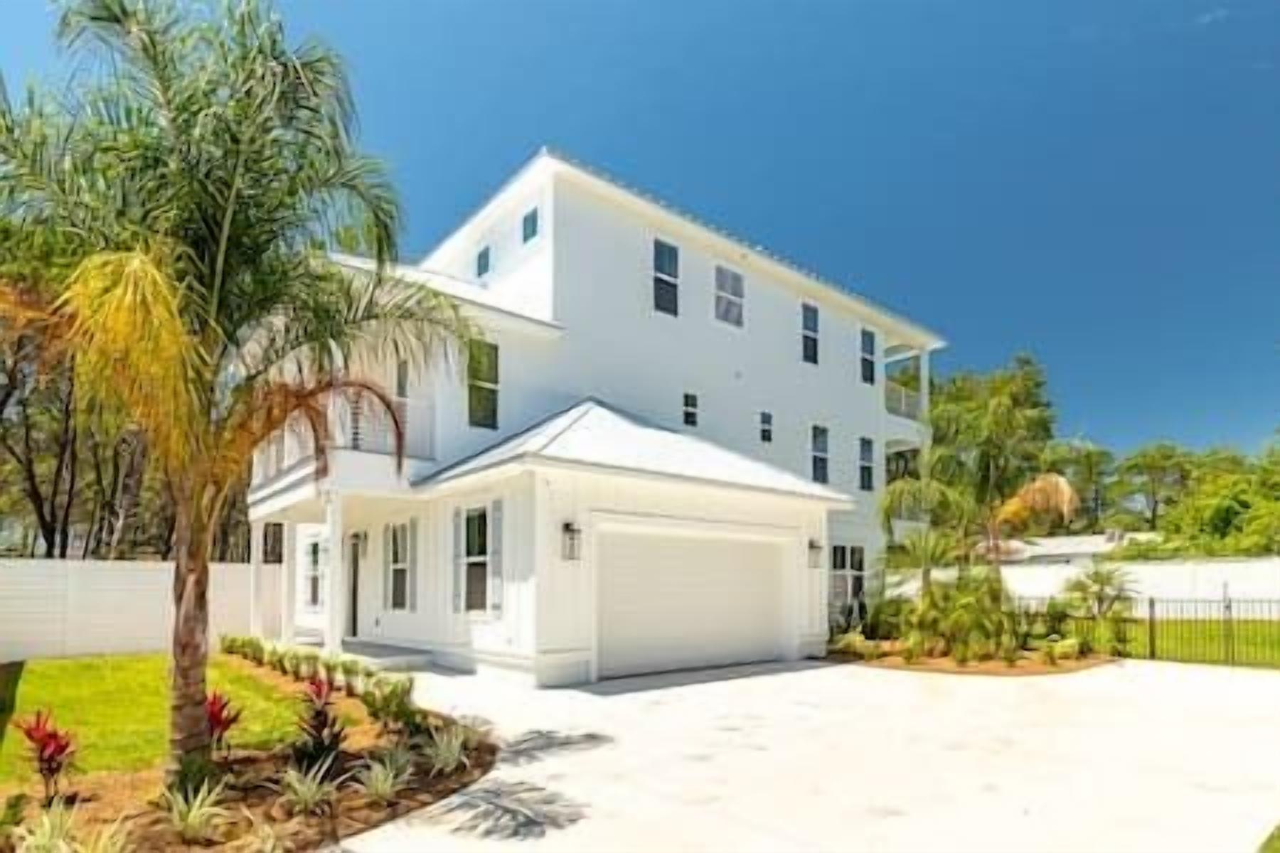 A two-story house with a white exterior, a garage, and a well-maintained garden with various plants and a palm tree.