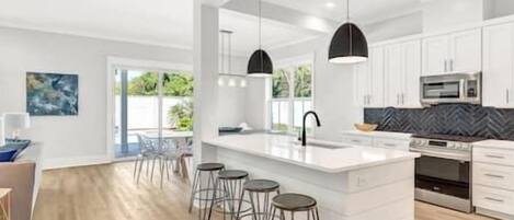 Una cocina moderna con una isla grande, taburetes de bar y electrodomésticos de acero inoxidable.